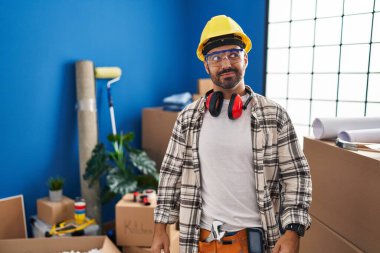Young hispanic man with beard working at home renovation smiling looking to the side and staring away thinking. 