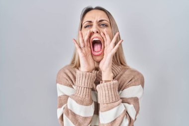 Sarışın bir kadın, izole edilmiş arka planda boğazlı kazak giyiyor ve elleri ağzında bağırıyor. 