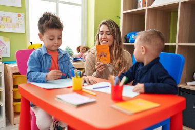 Teacher with boys sitting on table having language lesson at kindergarten