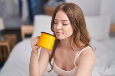 Genç bir kadın yatak odasında bir fincan kahve içiyor.