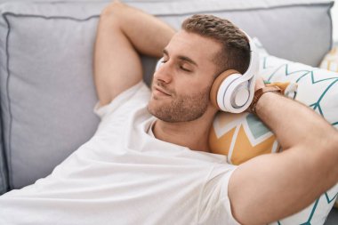 Young caucasian man listening to music lying on sofa at home