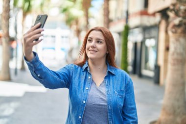 Young beautiful plus size woman smiling confident making selfie by the smartphone at street