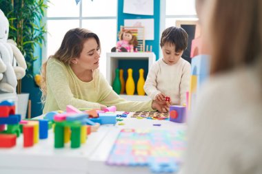 Teacher and toddler playing with maths puzzle game sitting on table at kindergarten