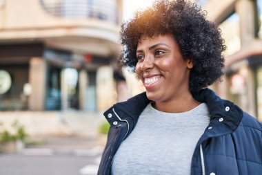 Afro-Amerikalı kadın gülümsüyor. Kendinden emin bir şekilde caddeye bakıyor.