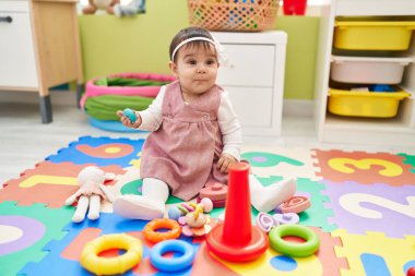 Anaokulunda elinde oyuncakla oturan sevimli İspanyol bebek.