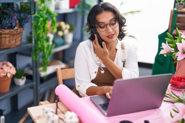 Çiçekçide dizüstü bilgisayar kullanarak konuşan güzel İspanyol çiçekçi kadın.