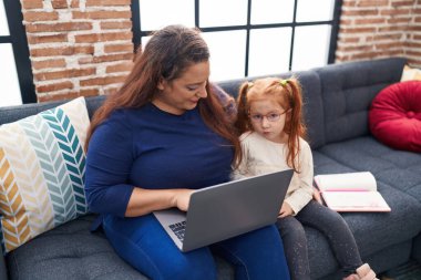 Teacher and student using laptop sitting on sofa at home
