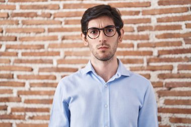 Young hispanic man standing over brick wall background skeptic and nervous, frowning upset because of problem. negative person. 