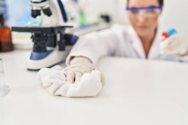 Young beautiful hispanic woman scientist cleaning table at laboratory