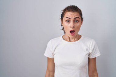Beautiful brunette woman standing over isolated background afraid and shocked with surprise and amazed expression, fear and excited face. 