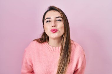Genç İspanyol kadın pembe arka planda dikilip kameraya bakıyor ve güzel ve seksi bir şekilde yayına öpücük yolluyor. aşk ifadesi. 