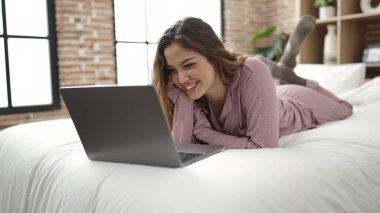 Yatakta dizüstü bilgisayar kullanan genç, güzel İspanyol kadın.