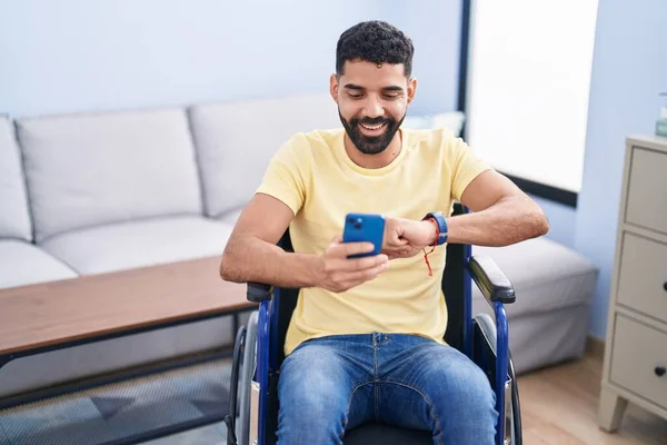 Young Arab Man Using Smartphone Looking Watch Sitting Wheelchair Home — ストック写真
