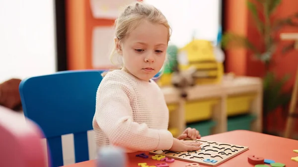 可爱的金发女孩坐在幼儿园的桌子上玩数学拼图游戏 — 图库照片