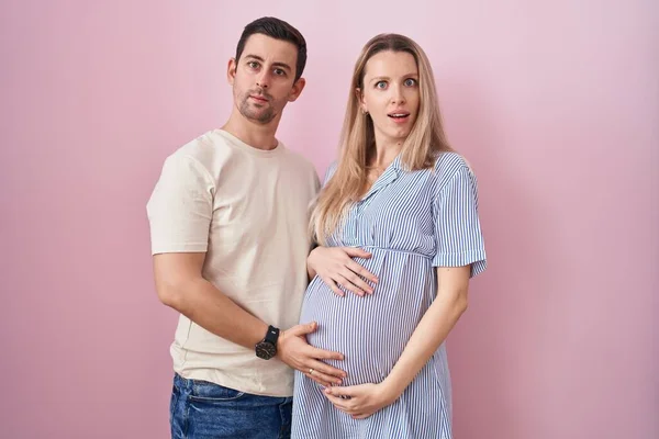 Casal Jovem Esperando Bebê Sobre Fundo Rosa Face Choque Olhando — Fotografia de Stock