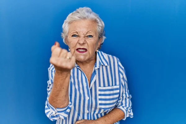 头发灰白的老妇人站在蓝色的背景上 怒气冲冲地举起拳头 怒气冲冲地大喊大叫 愤怒和好斗的概念 — 图库照片