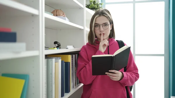 Young Blonde Woman Student Reading Book Doing Silence Gesture Library — Foto de Stock