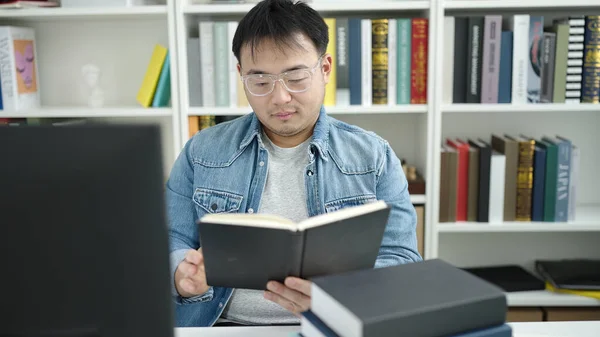 Young chinese man student reading book sitting on table at library university