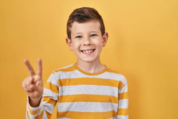 自信と幸せな笑みを浮かべている間 若い白人の子供は黄色の背景の上に立って指の数2を示すと指摘 — ストック写真