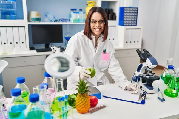 Young Beautiful Hispanic Woman Scientist Holding Apple Writing Document Laboratory — Stockfoto