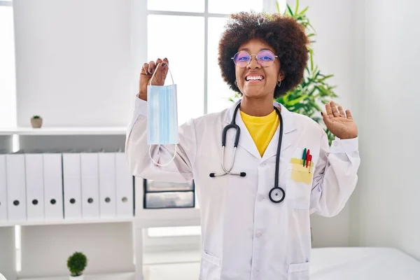 Young African American Woman Wearing Doctor Uniform Holding Safety Mask — Stock fotografie