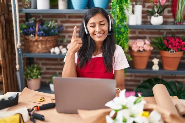 Young hispanic woman working at florist shop doing video call smiling with an idea or question pointing finger with happy face, number one
