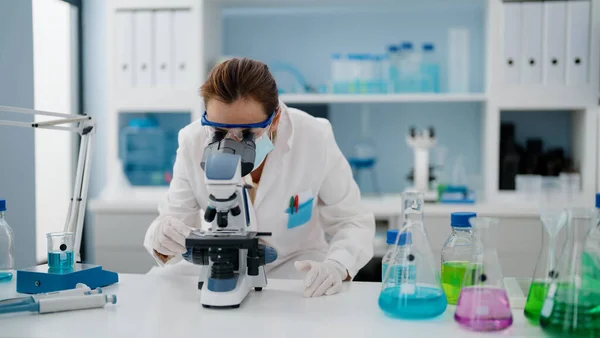 实验室显微镜下穿着科学家制服和医疗面具的中年恐慌女性 — 图库照片