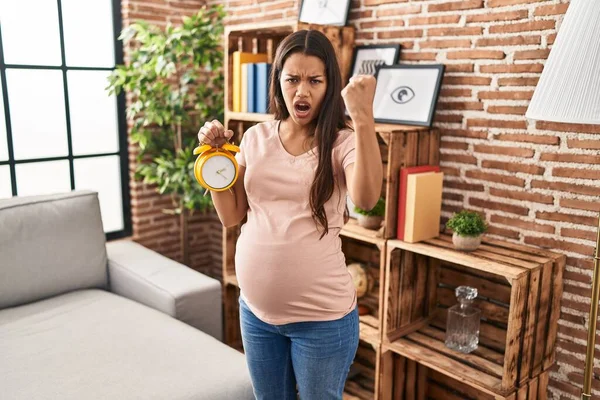 若いです妊娠中の女性のために目覚まし時計を持っています期限のためにいらいらし 怒りで叫びます 怒りと手を上げてクレイジー — ストック写真