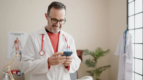 Middle age man doctor smiling confident using smartphone at clinic