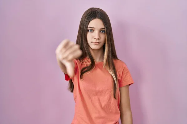 少女站在粉红的背景上 满脸愁容 怒气冲冲 以大拇指垂下的姿势表示拒绝和否定 不好的表达方式 — 图库照片