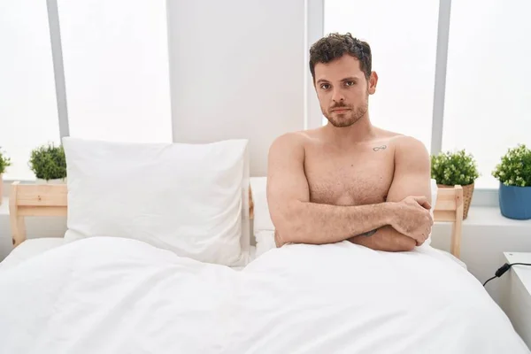 Young hispanic man unhappy sitting on bed at bedroom