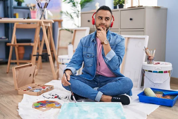 Young Hispanic Man Painter Sitting Floor Art Studio Serious Face — Foto de Stock