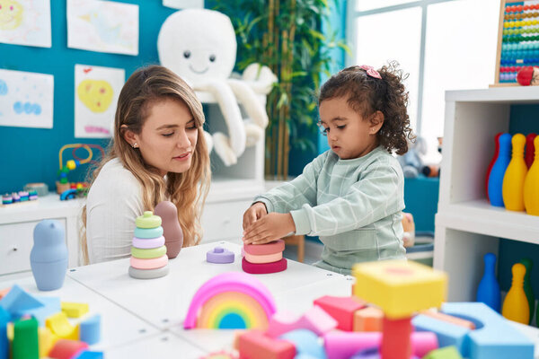Teacher and toddler playing with toys sitting on table at kindergarten
