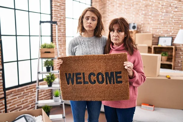 Mother and daughter holding welcome doormat depressed and worry for distress, crying angry and afraid. sad expression.