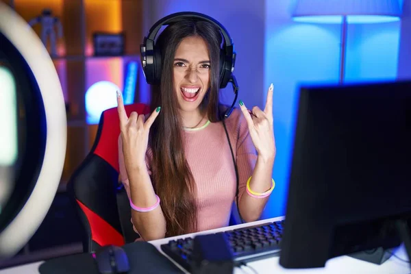 Young hispanic woman playing video games shouting with crazy expression doing rock symbol with hands up. music star. heavy concept.
