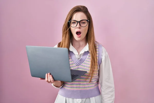 Young caucasian woman working using computer laptop angry and mad screaming frustrated and furious, shouting with anger. rage and aggressive concept.