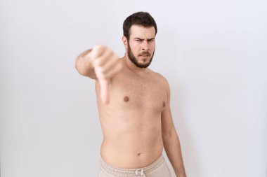 Beyaz arka planda üstsüz duran Latin asıllı genç adam mutsuz ve kızgın görünüyor. Reddedilmiş ve olumsuz hareketler yapıyor. kötü ifade. 