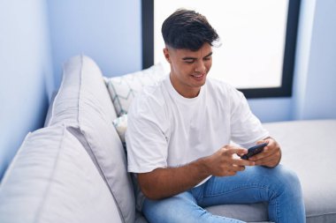 Evdeki kanepede oturan, akıllı telefon kullanan genç bir İspanyol.