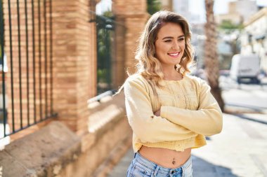 Kendine güvenen genç bir kadın caddede kollarını kavuşturmuş duruyor.