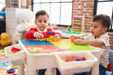 Two kids playing with construction blocks sitting on table at kindergarten