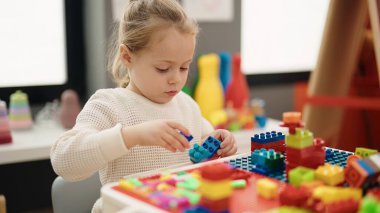 Adorable blonde girl playing with construction blocks sitting on table at kindergarten