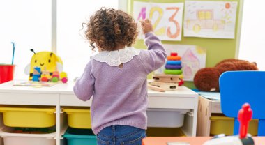 Adorable hispanic girl standing on back view at kindergarten