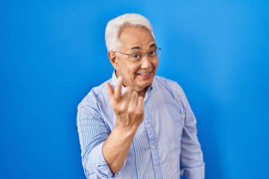 Hispanic senior man wearing glasses beckoning come here gesture with hand inviting welcoming happy and smiling 