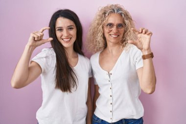 Anne ve kızı pembe arka planda bir arada duruyorlar gülümsüyorlar ve el hareketleriyle hareket ediyorlar parmaklarıyla işaret veriyorlar ve kameraya bakıyorlar. ölçüm kavramı. 
