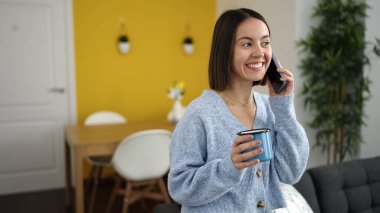 Genç, güzel, İspanyol bir kadın akıllı telefonda konuşuyor. Evde kahve içiyor.