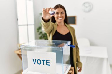 Young beautiful hispanic woman electoral table president holding vote badge at electoral college