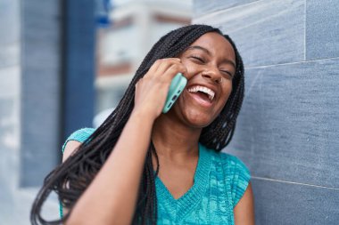 Afro-Amerikalı kadın gülümsüyor. Akıllı telefondan konuşuyor.