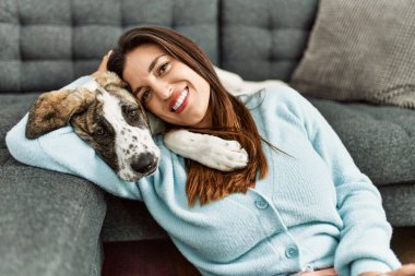 Genç kadın evde yerde oturan köpeğe sarılıyor.