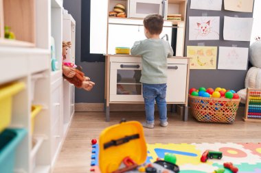 Adorable hispanic boy playing with play kitchen standing at kindergarten