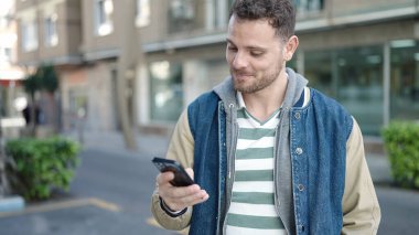 Young caucasian man smiling using smartphone at street